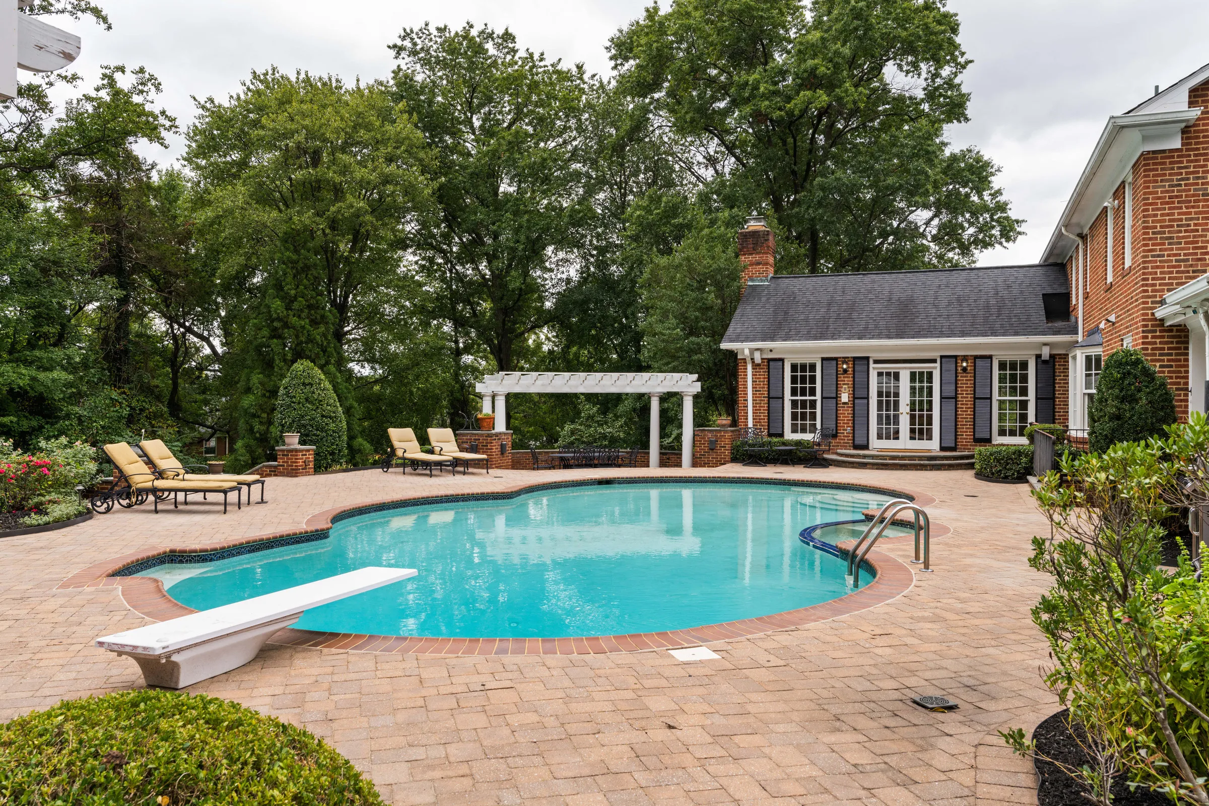 Before: a backyard pool with a diving board, loungers and a brick house under a flat, overcast sky