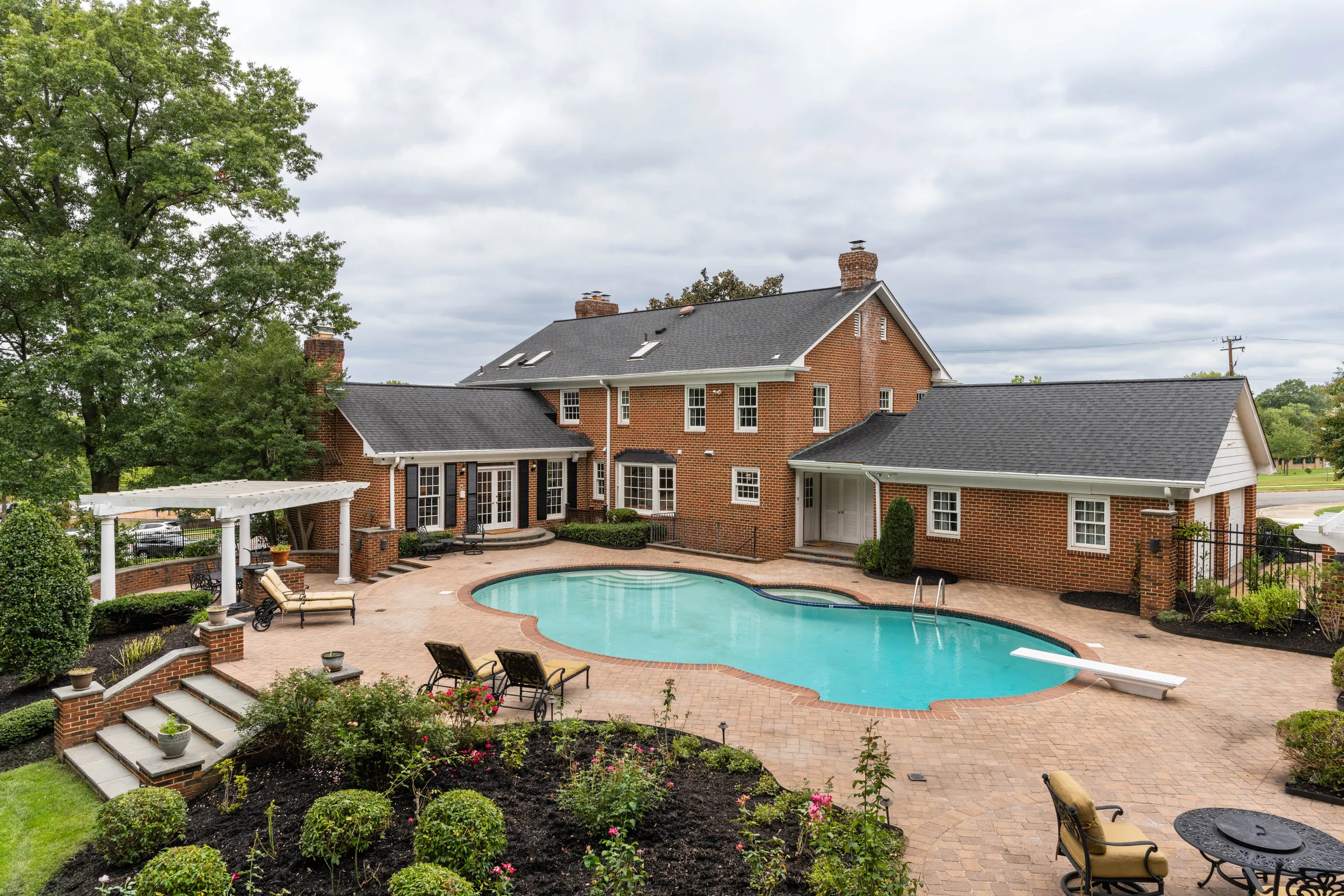 Before: the back of a brick colonial home with a pool and patio under a flat, overcast grey sky