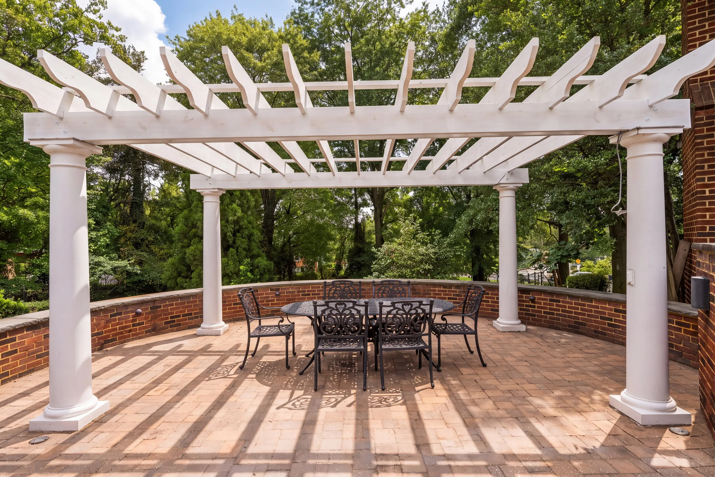 After: the same pergola in AI Studio with blue sky and sunlight casting the beams' shadows across the patio