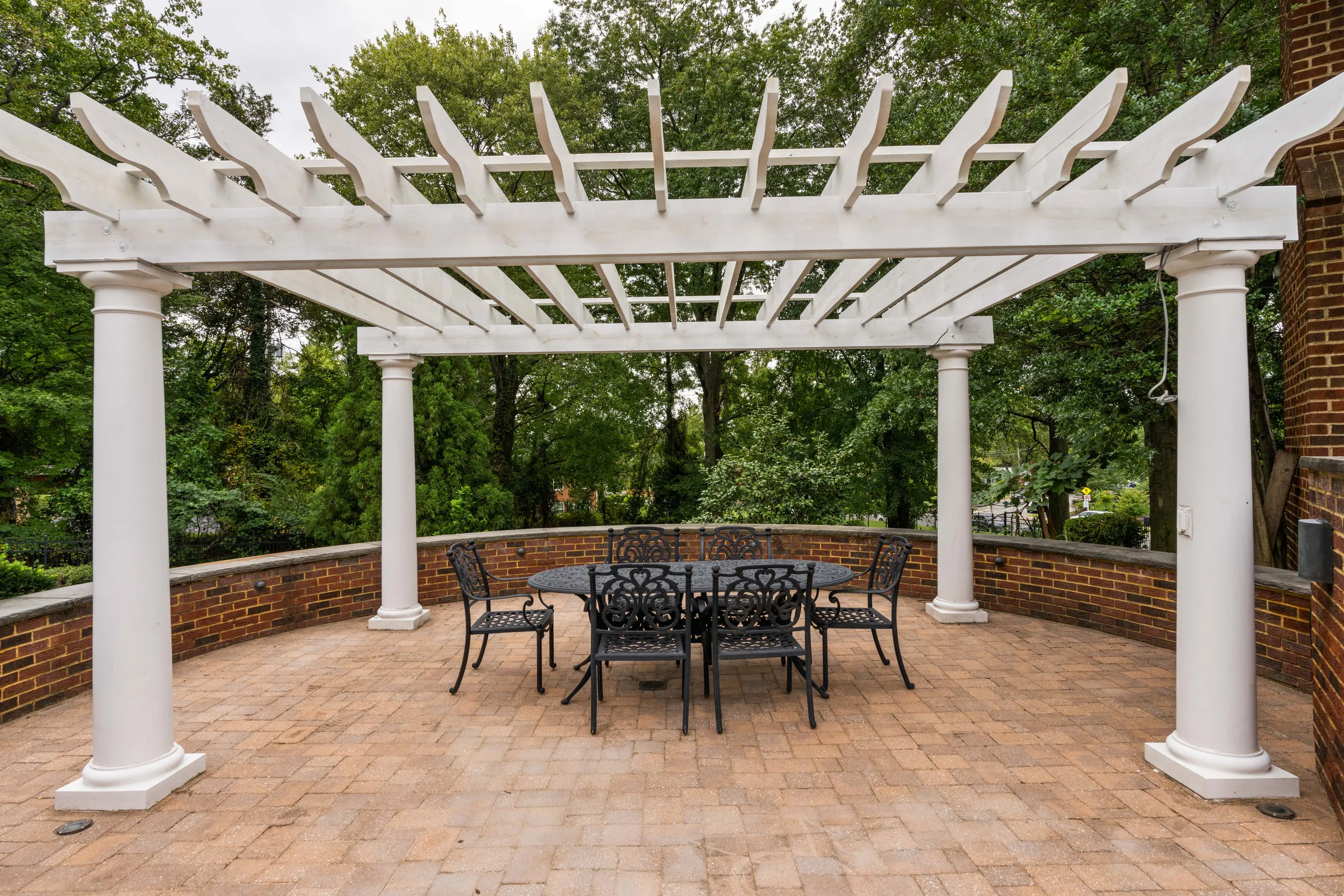 Before: a white pergola over a brick patio dining set on a flat, overcast day