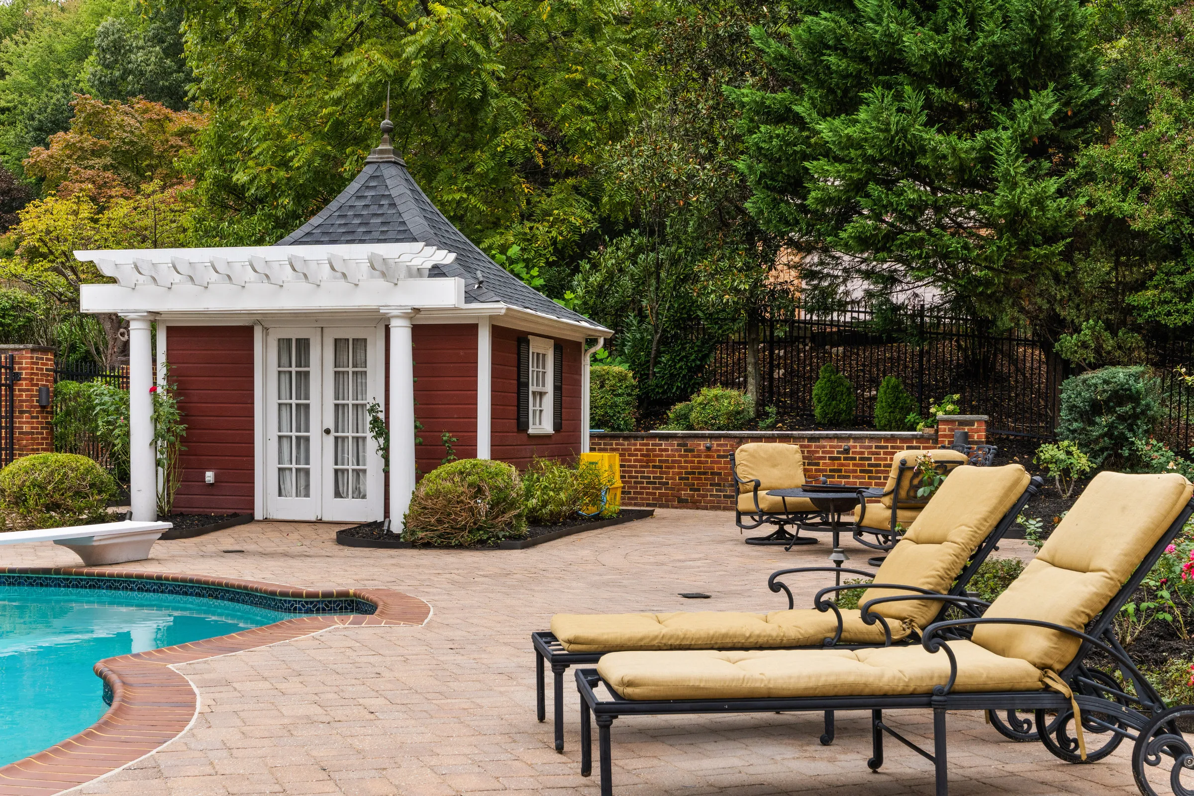 Before: a red pool house with a white pergola, patio loungers and trees on a grey, overcast day