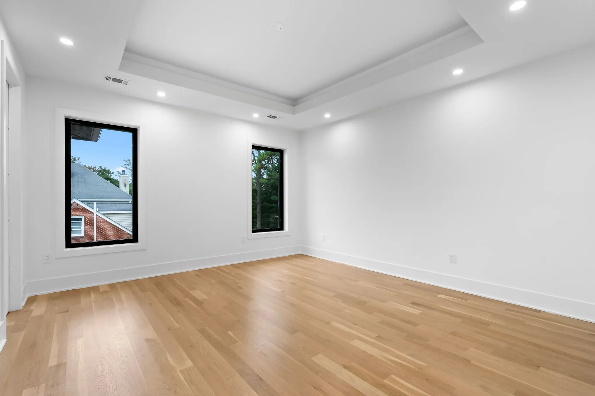 Before: an empty bedroom with oak floors, white walls, a tray ceiling and two tall black-framed windows