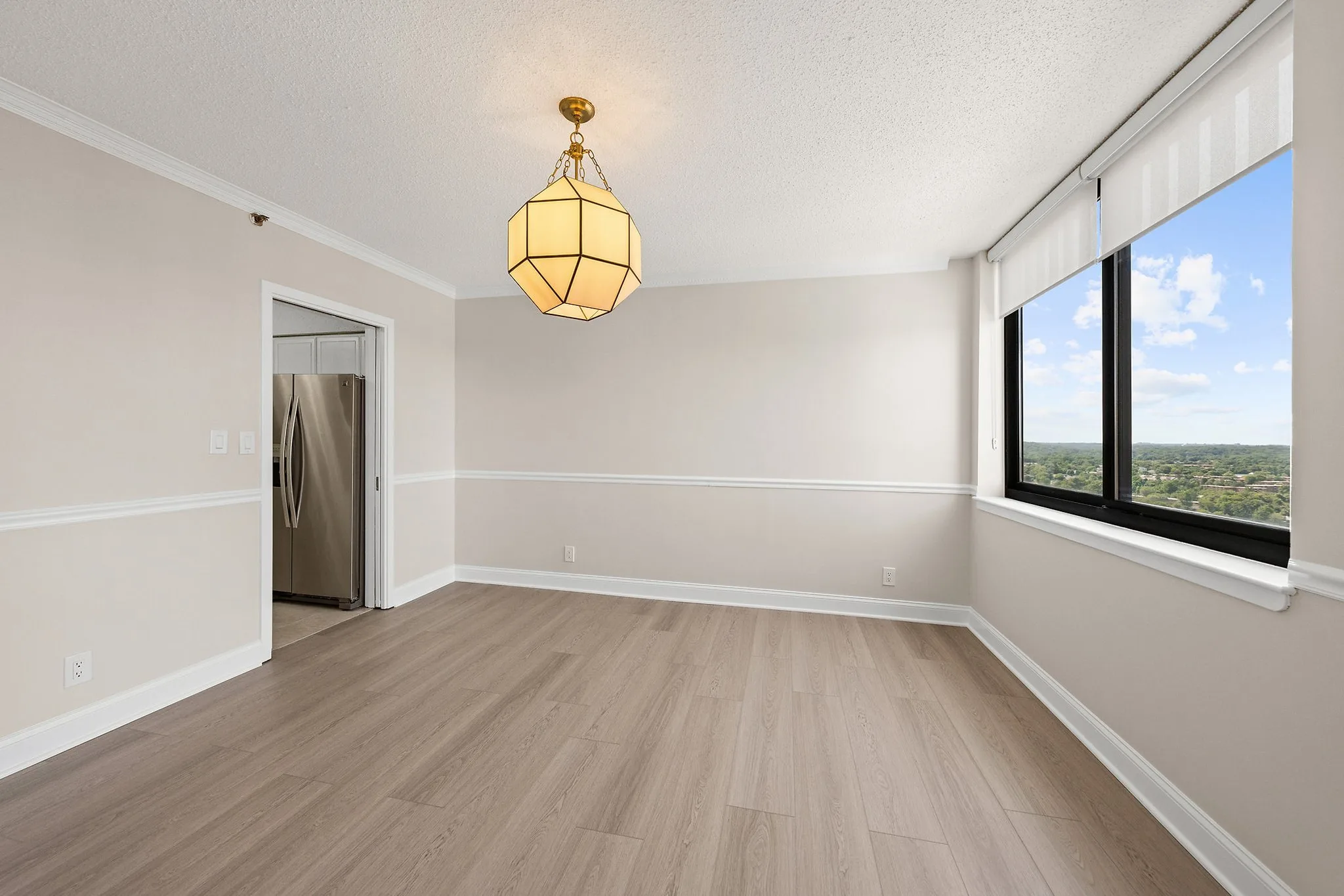 Empty dining room with a brass lantern pendant, chair rail, wood-look floors and a corner window over a wooded view