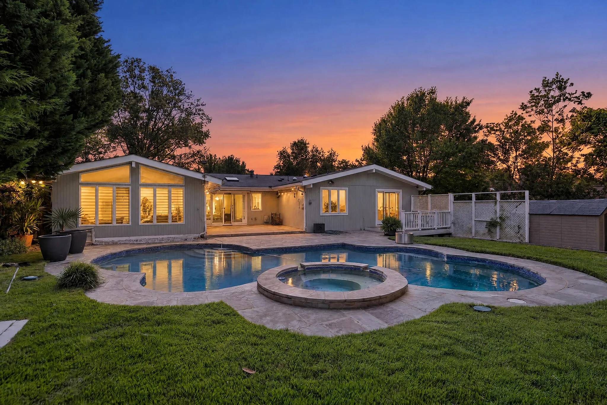 The same backyard as a virtual twilight: sunset sky, warm light in the windows and reflections in the pool