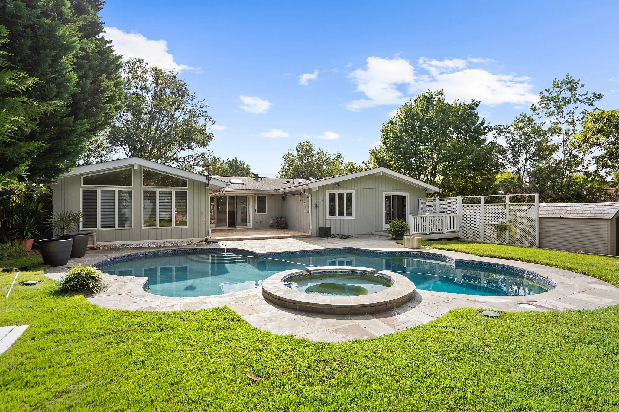 Backyard of a single-story home with a pool and hot tub on a sunny afternoon