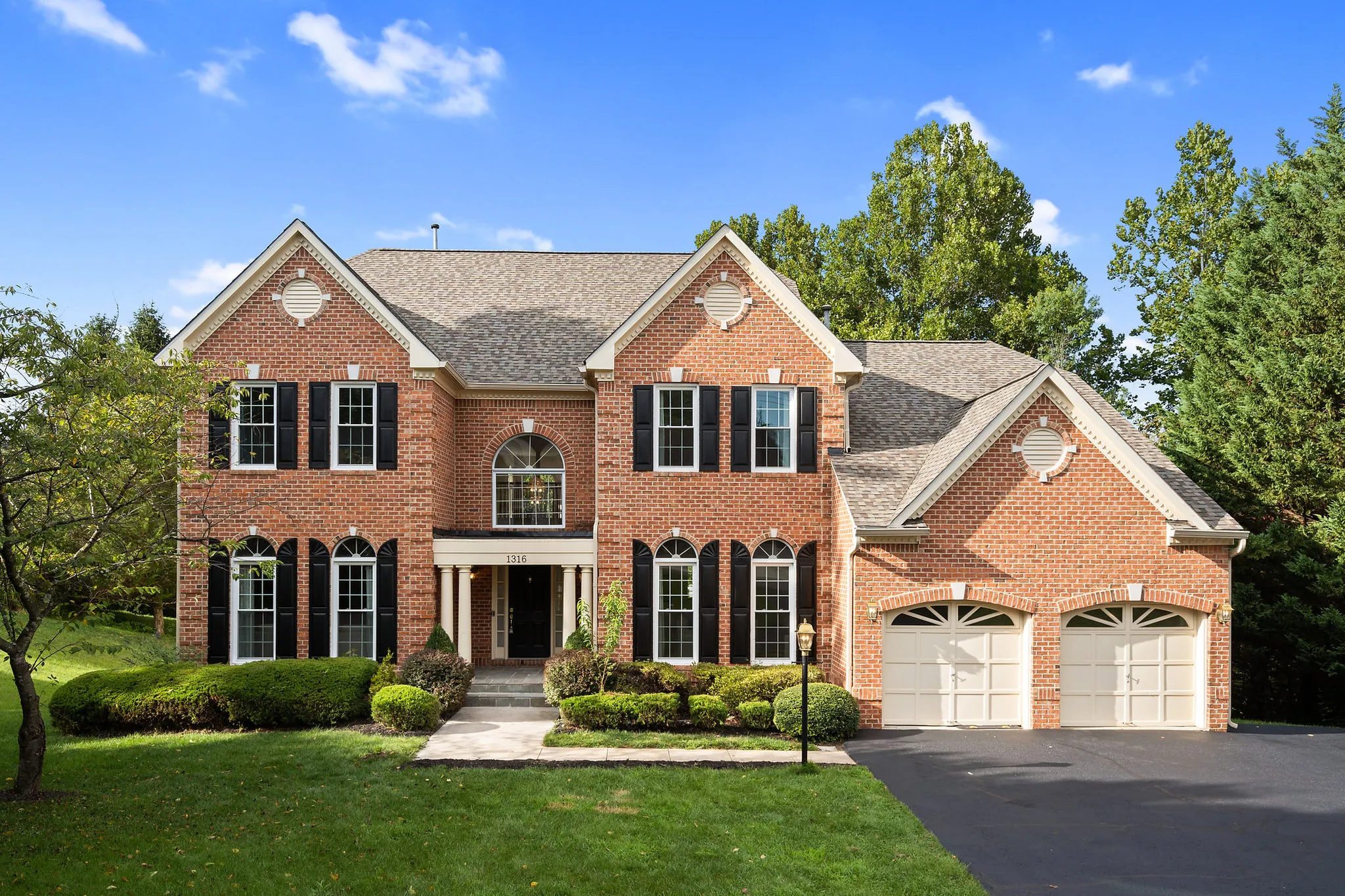 Before: the front of a two-story brick colonial with black shutters and a two-car garage on a sunny afternoon